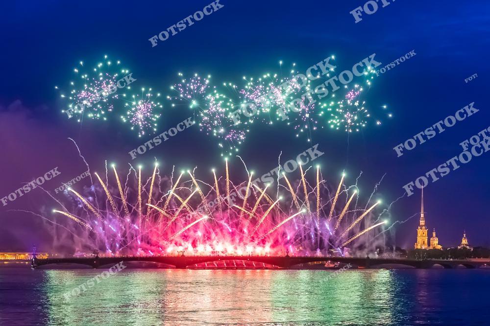 На фотографии изображен грандиозный салют в Санкт-Петербурге, развернувшийся над рекой Невой. Яркие разноцветные вспышки освещают ночное небо, создавая праздничную атмосферу. На заднем плане видна Петропавловская крепость с её узнаваемым шпилем. Отражения в воде добавляют дополнительный эффект и делают сцену ещё более впечатляющей.